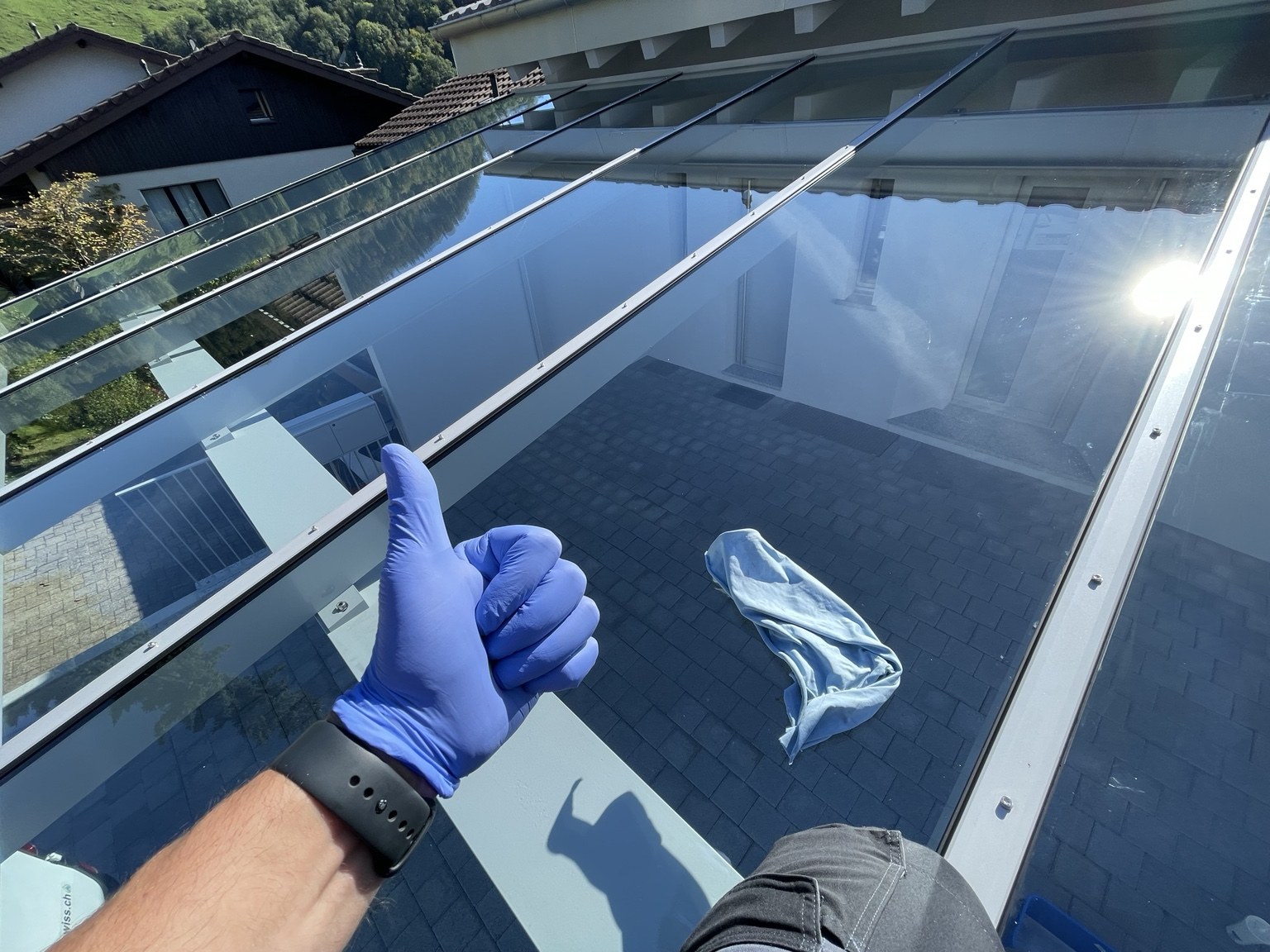 Gereinigtes Glasdach mit Spiegelung und einem Daumen nach oben im blauen Arbeitshandschuh