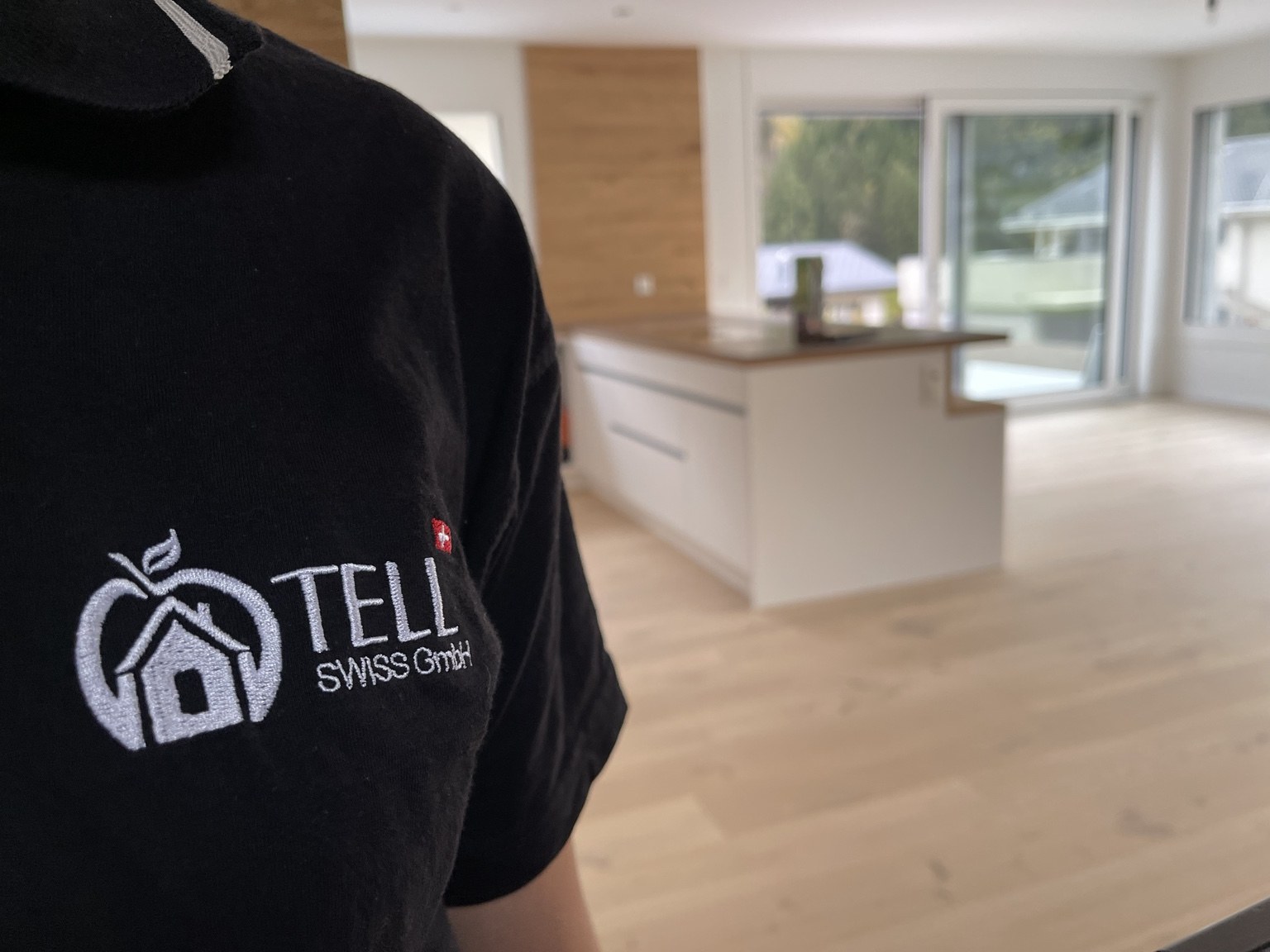 Tell Swiss Firmenlogo auf Arbeitskleidung vor einer leeren Wohnung mit offener Küche
